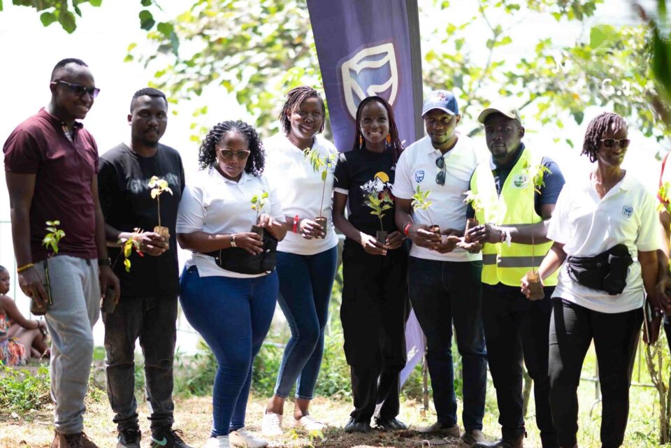 Stanbic Bank team led by Saulo Nabende 3RD Right and Vumbula team led by Peter Ssebulime 2nd Left pose for a group photo with Hon. Barnard Odoi ahead of the tree planting session. 11zon